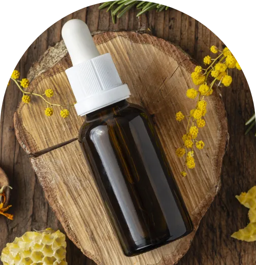 Braunes Glasfläschchen mit Pipette, auf einem Holzuntergrund liegend, umgeben von gelben Blüten – symbolische Darstellung von Bachblüten-Essenzen.